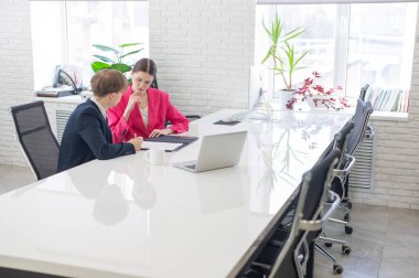 Kadın ve erkek ofiste otururken konuşuyorlar.