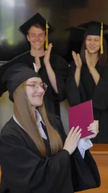 Sınıf arkadaşları onu alkışlarken, elinde diploma tutan beyaz bir kadın.