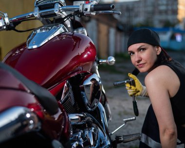 Esmer kadın kırmızı bir motosikleti tamir ediyor.