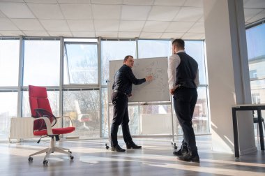 Beyaz bir kurulda iş tartışan iki beyaz adam.