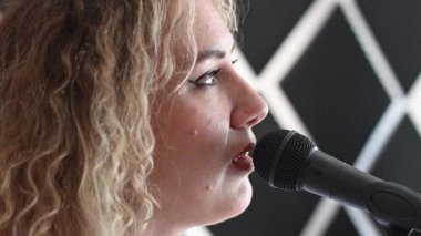 Beyaz kadın müzik stüdyosunda mikrofona şarkı söylüyor.