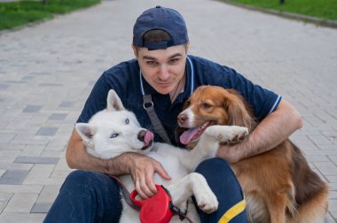 Bir adam yürürken iki köpeğini kucaklıyor.