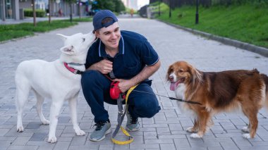 Bir adam yürürken iki köpeğini kucaklıyor.
