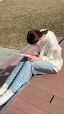 Açık havada kalemle çizim yapan beyaz bir kadın.