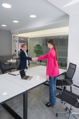 Beyaz erkek ve kadın ofiste selamlaşıp el sıkışıyor.