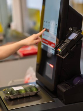 Bir kadın self-servis kasasında salatalık tartır.