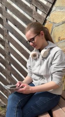 Genç bir kadın bankta otururken akıllı telefon kullanıyor.