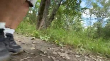 Bir adam ormanda bir patika boyunca yürür. Erkeklerin bacaklarına yakın çekim.