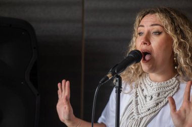 Beyaz kadın müzik stüdyosunda mikrofona şarkı söylüyor.