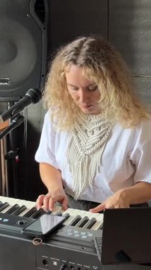 Beyaz kadın mikrofona şarkı söylüyor ve sentezleyici çalıyor. Akıllı telefondaki notlara bakıyorum.