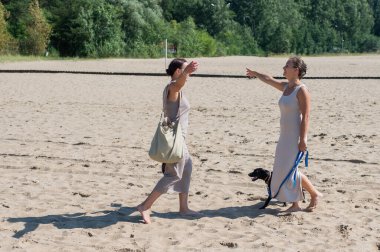 Kumsalda bir köpekle yürüyen iki beyaz kadın.