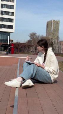 Açık havada kalemle çizim yapan beyaz bir kadın.