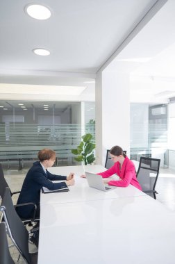 Kadın ve erkek ofiste otururken konuşuyorlar.