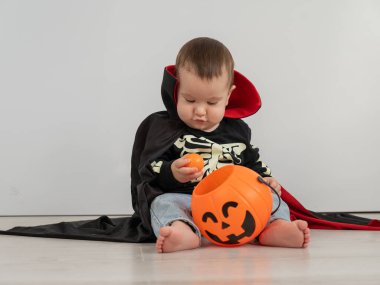 Beyaz arka planda şeker sepeti tutan Dracula Cadılar Bayramı kostümlü beyaz tatlı çocuk.