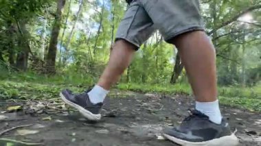 Bir adam ormanda bir patika boyunca yürür. Erkeklerin bacaklarına yakın çekim.