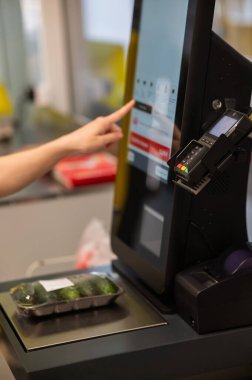 Bir kadın self-servis kasasında salatalık tartır.