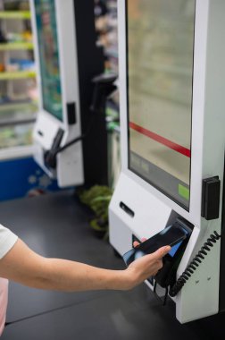 Bir kadın kendini kontrol ederken akıllı telefonuyla ödeme yapar.