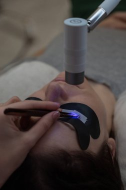 Kirpik uzatma prosedüründen geçen bir kadın ultraviyole lamba kullanıyor.