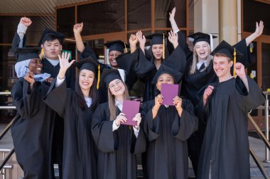 Farklı uluslardan mutlu öğrenciler mezuniyet elbiseleriyle diplomalarını tutuyorlar.