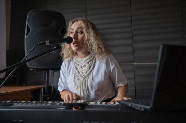 Beyaz kadın mikrofona şarkı söylüyor ve sentezleyici çalıyor.