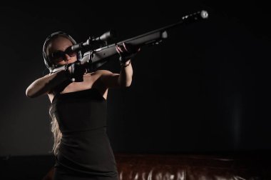 Beyaz bir kadın tüfek ve dürbünle atış talimi yapıyor.