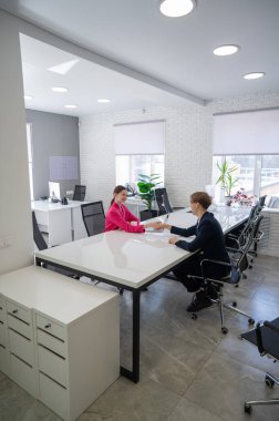 Beyaz erkek ve kadın ofiste selamlaşıp el sıkışıyor.