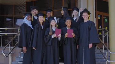 Farklı uluslardan mutlu öğrenciler mezuniyet elbiseleriyle diplomalarını tutuyorlar.