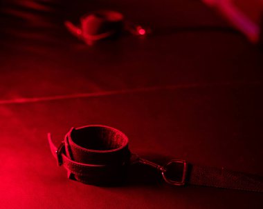 Kırmızı ışık altında BDSM oyunları için deri kelepçelerin yakın plan çekimi