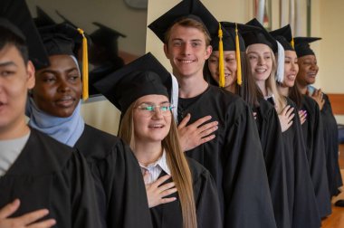 Mezunlar törende gururla dururlar. Elleri kalplerinin üstünde.