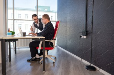 Beyaz adam çalışma masasında durmuş iş hakkında konuşuyor.