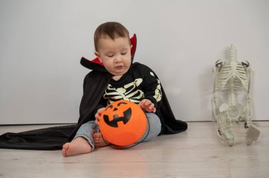 Beyaz arka planda şeker sepeti tutan Dracula Cadılar Bayramı kostümlü beyaz tatlı çocuk.