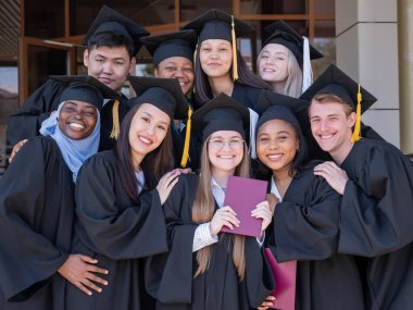 Farklı uluslardan mutlu öğrenciler mezuniyet elbiseleriyle diplomalarını tutuyorlar.