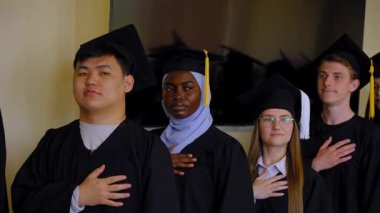 Mezunlar törende gururla dururlar. Elleri kalplerinin üstünde.