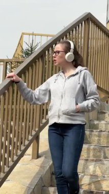 Genç bir kadın yürürken kablosuz kulaklıkla müzik dinliyor.