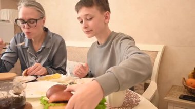 Orta yaşlı beyaz bir kadın oğluyla yemek yiyor.