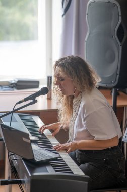 Beyaz kadın mikrofona şarkı söylüyor ve sentezleyici çalıyor. Bilgisayarda çevrimiçi ders