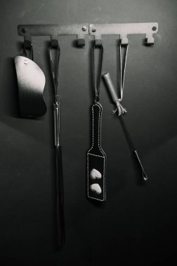 Duvarda bir dizi BDSM aksesuarı asılı.