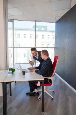 Beyaz adam çalışma masasında durmuş iş hakkında konuşuyor.