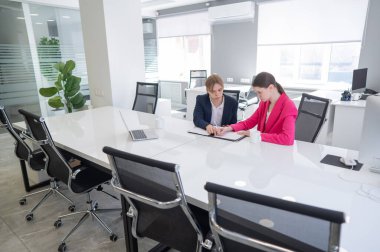 Kadın ve erkek ofiste otururken konuşuyorlar.