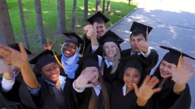 Mezuniyet elbisesi giymiş farklı uluslardan öğrenciler ellerini sallıyor.