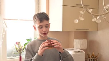 Bir çocuk mutfakta ev yapımı bir burger yiyor.