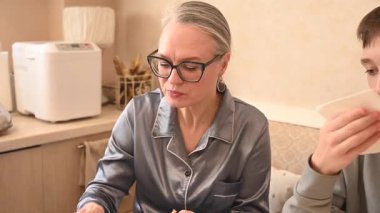 Orta yaşlı beyaz bir kadın oğluyla yemek yiyor.