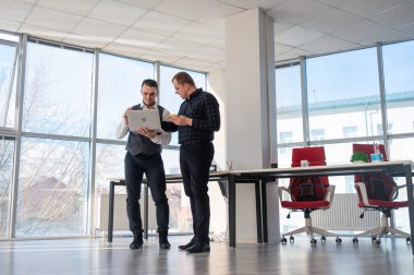 İki beyaz adam dizüstü bilgisayara bakıyor ve iş tartışıyorlar.