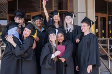 Farklı uluslardan mutlu öğrenciler mezuniyet elbiseleriyle diplomalarını tutuyorlar.