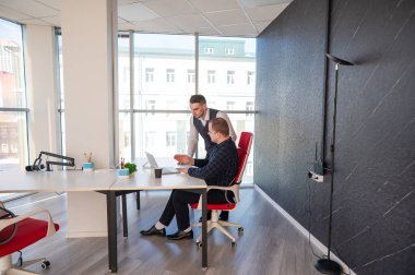 Beyaz adam çalışma masasında durmuş iş hakkında konuşuyor.