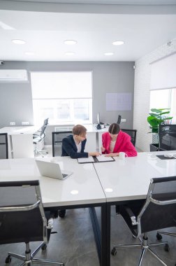 Kadın ve erkek ofiste otururken konuşuyorlar.