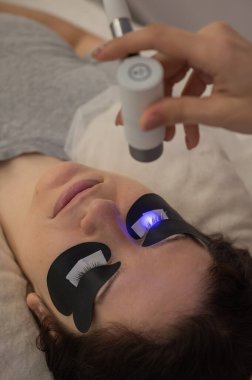 Kirpik uzatma prosedüründen geçen bir kadın ultraviyole lamba kullanıyor.