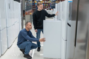 İki beyaz adam bir hırdavatçıdan buzdolabı seçiyor.