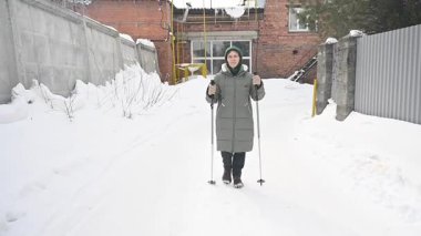 Kafkasyalı yaşlı kadın kışın İskandinav bastonlarıyla yürüyor