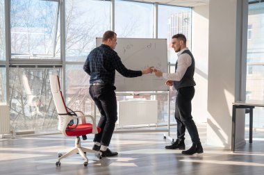 Beyaz bir kurulda iş tartışan iki beyaz adam.